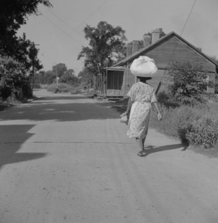 Woman Carrying Sack of Laundry on her Head along Dirt Road, Rear View, Natchez, Mississippi, USA, Marion Post Wolcott for Farm Security Administration, August 1940