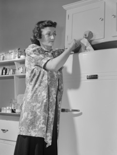 Woman Using Slip of Paper to see if Refrigerator is Wasting Valuable Electric Power and if the Paper can be Pulled out, have the Gasket Tightened or Replaced Immediately and Help Uncle Sam Conserve En...