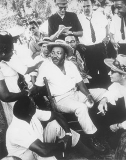 Martin Luther King, Jr in Straw Hat Sitting Down with Group of Men While Shaking Hands with Woman, circa 1960's