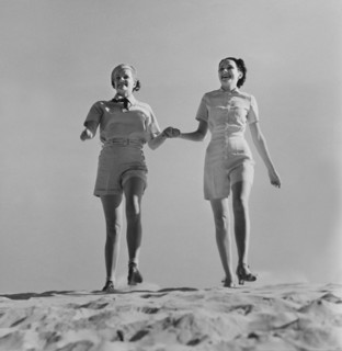 Two Fashionable Women in Shorts Holding Hands While Walking on Beach, circa 1952
