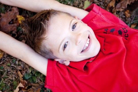 Smiling Boy With Arms Above Head Laying on Ground, High Angle View