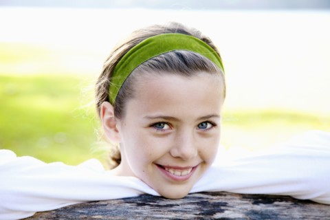 Smiling Girl Wearing Green Headband with Chin Resting on Fence