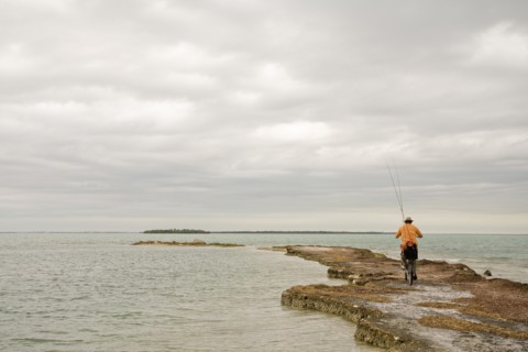 Man Riding Bicycle With Fishing Rods on Beach, Florida Keys, USA
