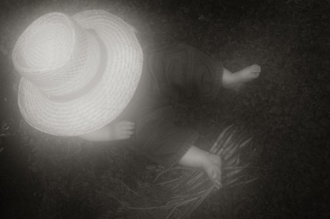 Young Boy in Large Hat Sitting on Ground with Carrots, High Angle View