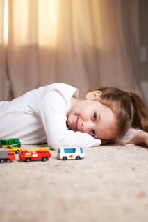 Smiling Girl Portrait on Floor with Toy Cars and Trucks
