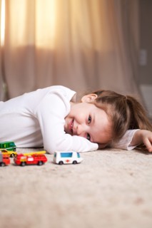 Smiling Girl Portrait on Floor with Toy Cars and Trucks
