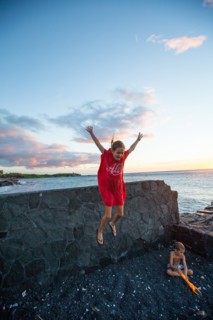 Young Girl Jumping off Lava Rock Wall while her Brother is Playing in  Black Sand at Ocean Beach, Hawaii, USA