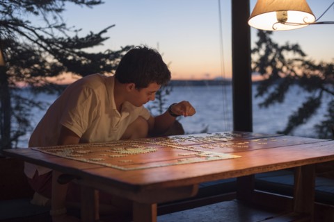 Teenage Boy Doing Jigsaw Puzzle at Lake House at Sunset