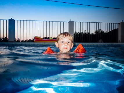 Young Boy floating in Swimming Pool at Sunset,