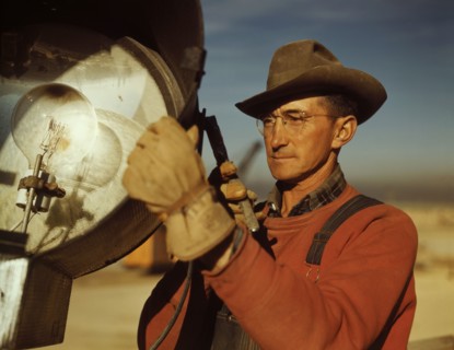 Man servicing floodlight at new construction of steel plant being built to aid war effort of steel production