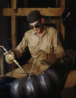Welder gas welding a joint in a line of spiral pipe