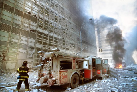 New York City fire fighter pulling water hose from fire truck amid debris and burning buildings following September 11th terrorist attack on World Trade Center