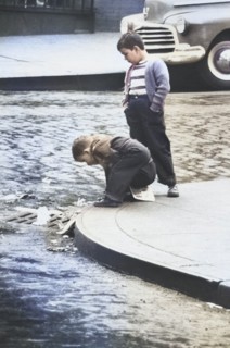Two Young Boys on Street Corner looking in Storm Drain
