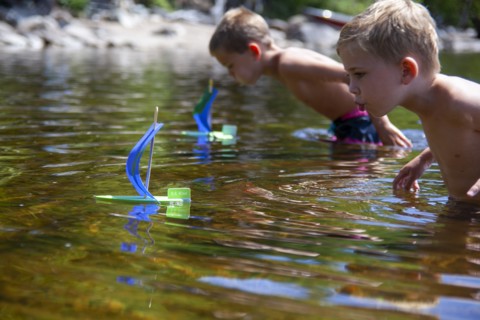 Two young boys with homemade toy sailboats in lake