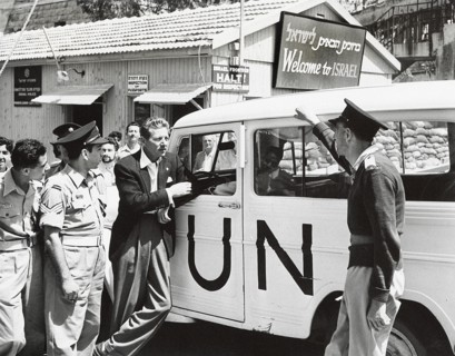 Danny Kaye leaning against UN vehicle near sign saying "Welcome to Israel"
