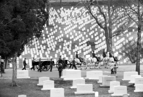 Flag-draped casket carried by horse-drawn caisson during a funeral