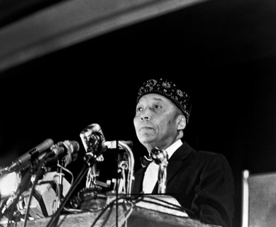 Elijah Muhammad standing behind microphones at podium