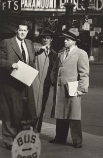 Three businessmen in overcoats talking on sidewalk