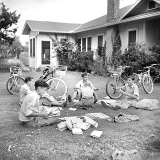 Group of boys folding newspapers on front yard lawn before delivering them in the afternoon,