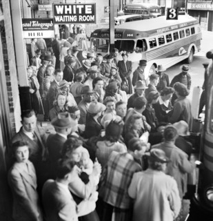 Crowded bus terminal with "White Waiting Room" sign in foreground and "Colored Waiting Room" in
