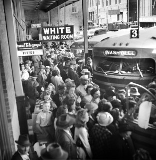 Crowded bus terminal with "White Waiting Room" sign in foreground and "Colored Waiting Room" in