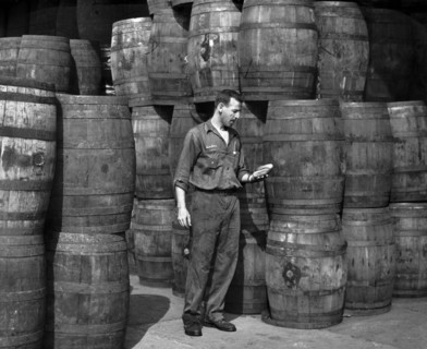 Stanley Hyams, co-owner of Washington Pickle Works, holding two pickles in a room full of barrels