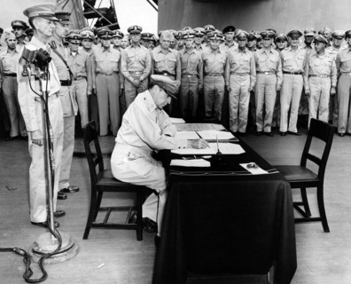 U.S. General Douglas MacArthur seated at desk during formal surrender ceremonies aboard USS