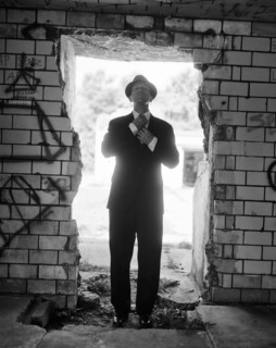 Mid-adult man in suit and hat adjusting tie while standing in open doorway