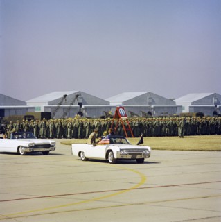 U.S. President John Kennedy riding in open convertible car past soldiers in review formation while
