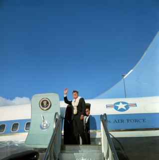 U.S. President John F. Kennedy (wearing flower leis) waving to crowd from stairs of Air Force One