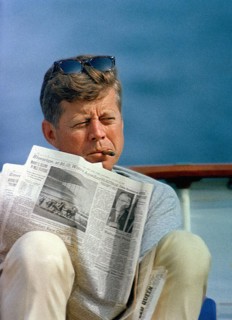 U.S. President John F. Kennedy smoking cigar and reading newspaper while sitting aboard