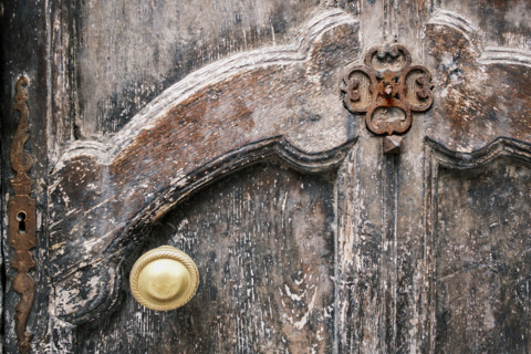 Weathered wood door with intricate carvings, rusted metal hardware and gold-colored door knob