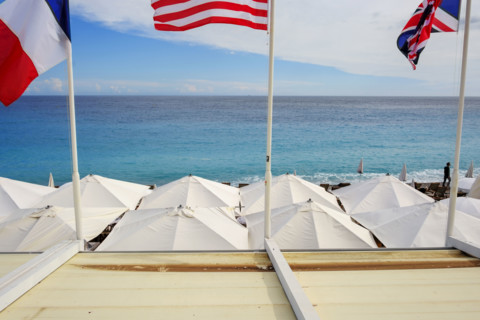 Beach umbrellas and Franch, American and British flags at beach club on Mediterranean Sea, Nice,