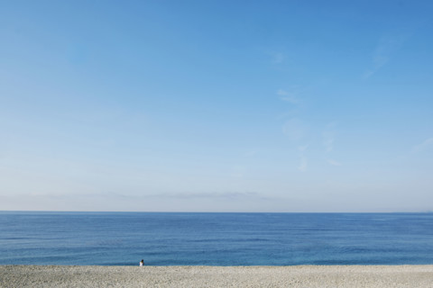 Rear view of solitary woman sitting on beach and looking out to sea