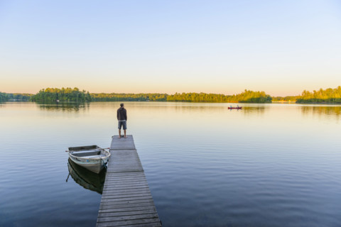 Rear view of teen boy standing at end of dock and looking out to lake