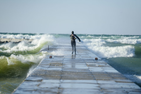 Rear view of surfer in wetsuit walking to end of pier