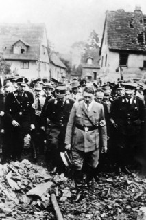 Adolf Hitler, accompanied by other German officials, grimly inspecting bomb damage in German city,