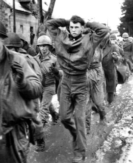 U.S. soldier with hands clasped behind his head, leading a file of American prisoners captured by