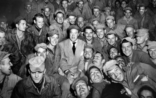Bob Hope, radio and screen star, sitting with men of X Corps, as members of his troupe entertain,