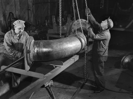 Two factory workers fitting flange on huge pipe, Bethlehem-Fairfield shipyards, Baltimore,