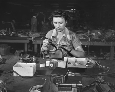 Female worker soldering contact point on end of wire, De Soto bomber plant, Detroit, Michigan, USA,