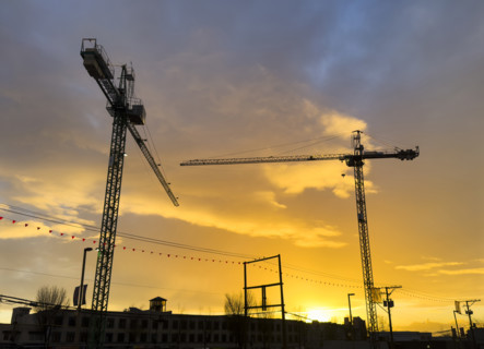 Two silhouetted construction cranes at sunset