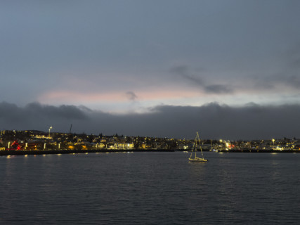 Sailboat with Christmas lights in harbor with illuminated seaside town in background,