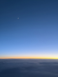 Crescent moon in deep blue sky at sunset viewed through airplane window