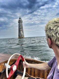 Young adult man driving vintage motor boat near lighthouse