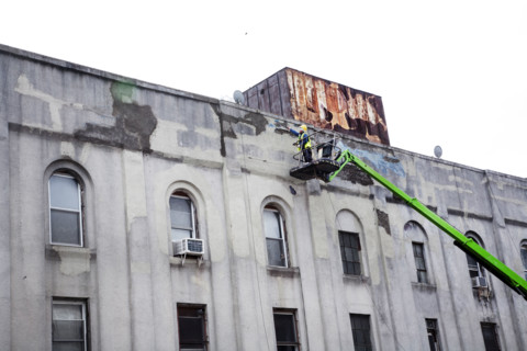 Workman repairing facade of old factory building, Brooklyn, NY, USA