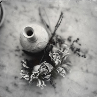 Empty vase with pile of dried flowers by its side
