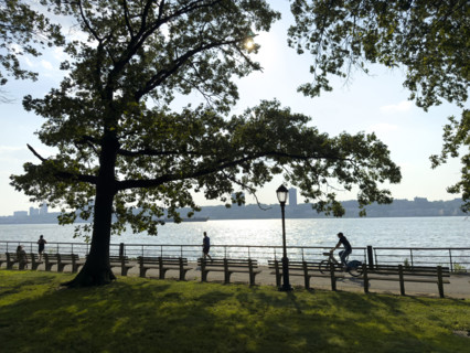 Joggers and bicyclist on westside bike path along Hudson River with view of New Jersey in background, Manhattan, New York City