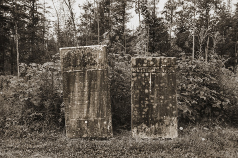 Two weathered headstones at edge of cemetery