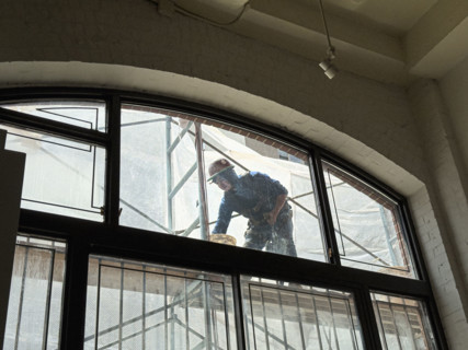 Construction worker repairing building façade, viewed through residential apartment window,